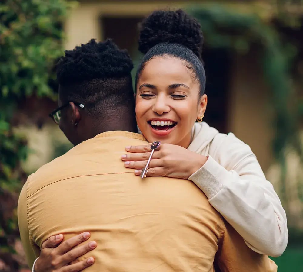 Couple Hugging in front of a house with a house key in the lady's hand