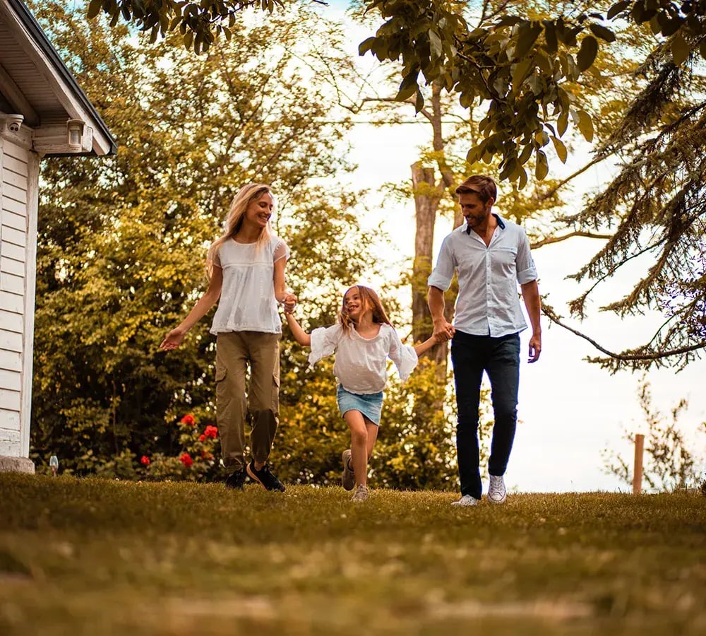 A happy young girl skipping in the yard, holding her mom's and dad's hands