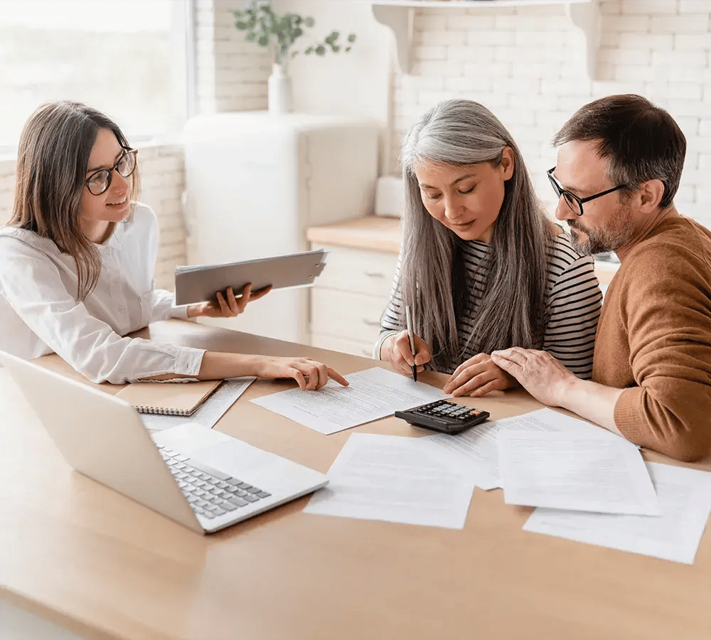 Three people sitting around a desk and carefully reviewing documents