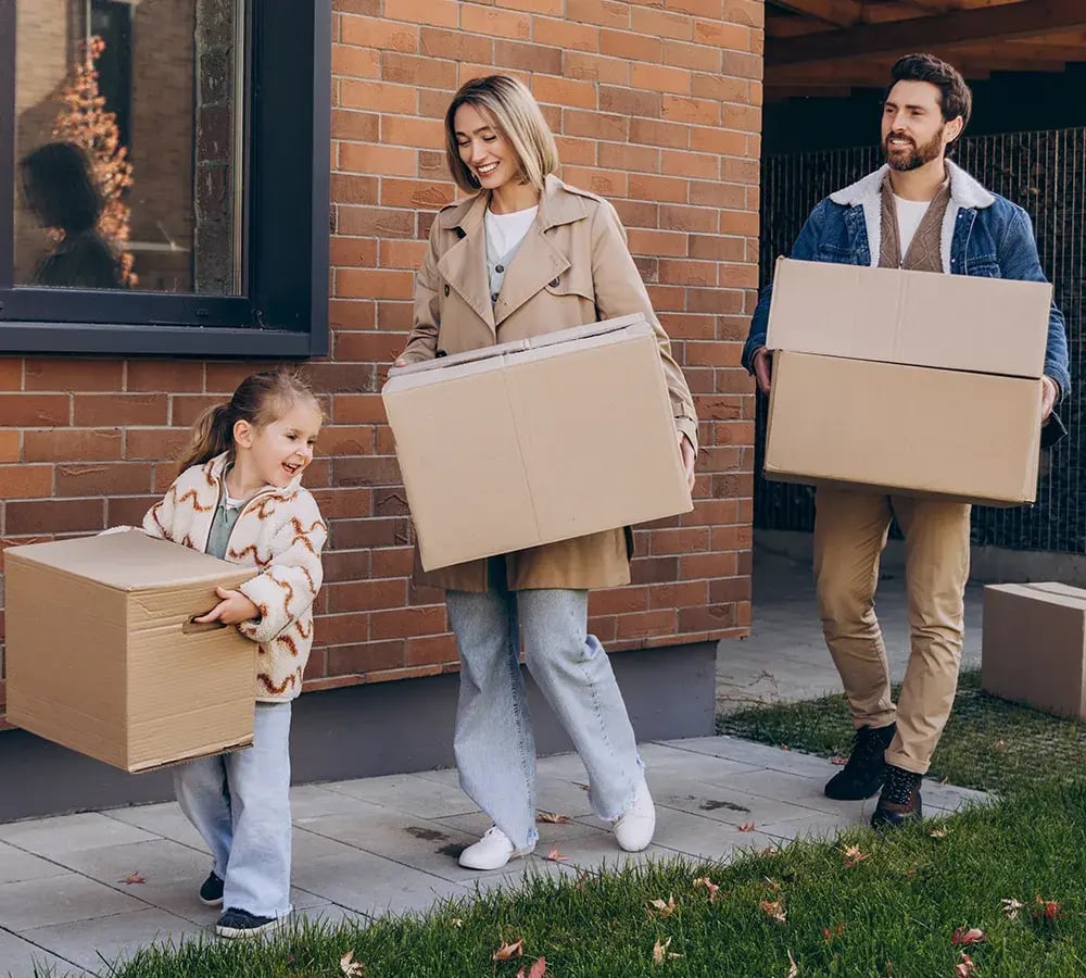A young girl and her parents are happily carrying moving boxes into a home